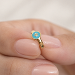 Gold-tone hoop with a turquoise-blue round face and a gold-tone star held between fingers.