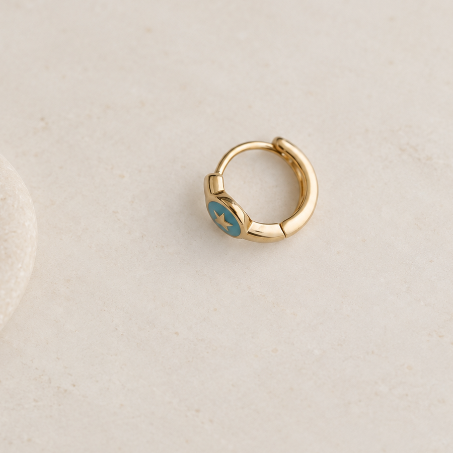 Gold-tone hoop with a turquoise-blue star face on a pale surface, shown with the clasp closed.