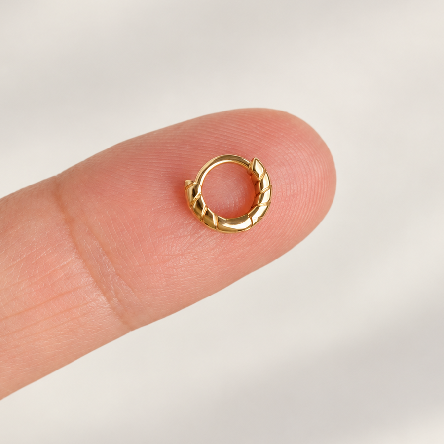 Small gold-tone hoop with diagonal grooves resting on a fingertip.