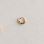 Gold-tone grooved hoop with its clasp closed on a pale surface beside a pebble.