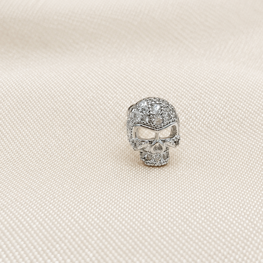 Silver-tone skull stud earring with clear stones on folded white fabric.