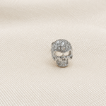 Silver-tone skull stud earring with clear stones on folded white fabric.