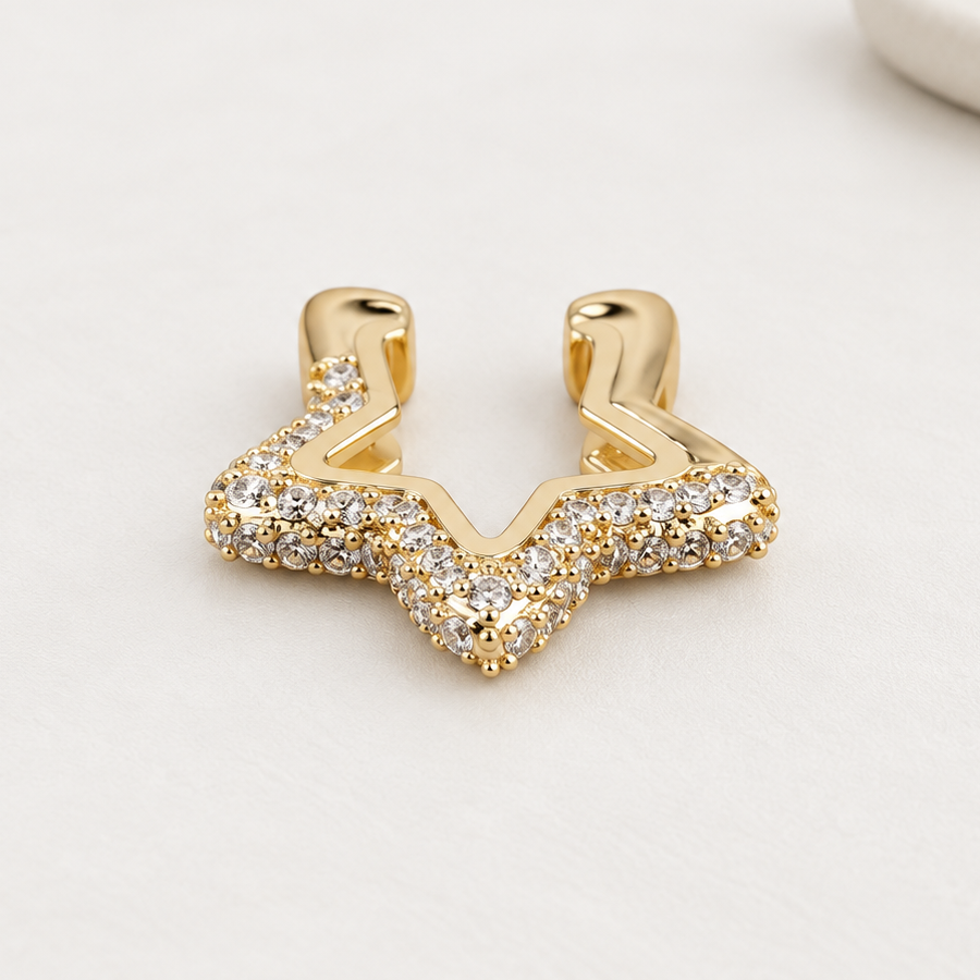 Gold-tone star-shaped ear cuff with clear stones on a white surface, showing the open ends.