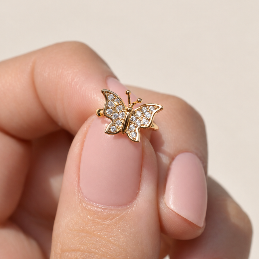 Gold-tone butterfly ear cuff held between fingers, showing clear stones across its wings.