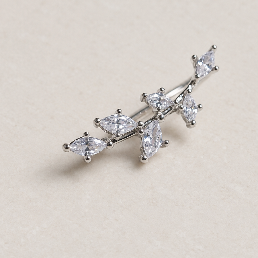 Silver-tone branch-shaped ear jewellery with clear leaf-shaped stones on a pale surface.