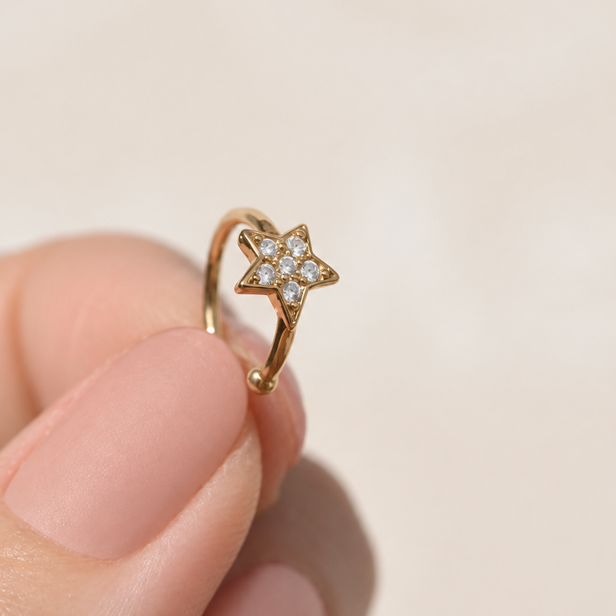 Gold-tone ear cuff held between fingers, with a small clear-stone star and an open band.