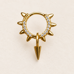 Gold-coloured clear-stone hoop with pointed outer spikes and a hanging spike charm on a pale surface.