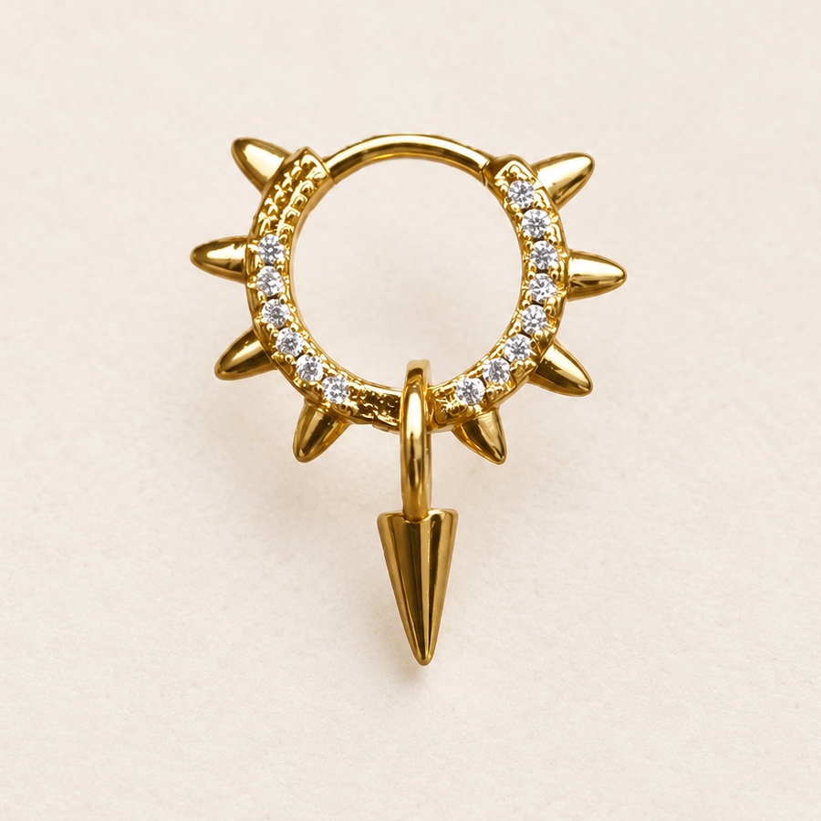 Gold-coloured clear-stone hoop with pointed outer spikes and a hanging spike charm on a pale surface.