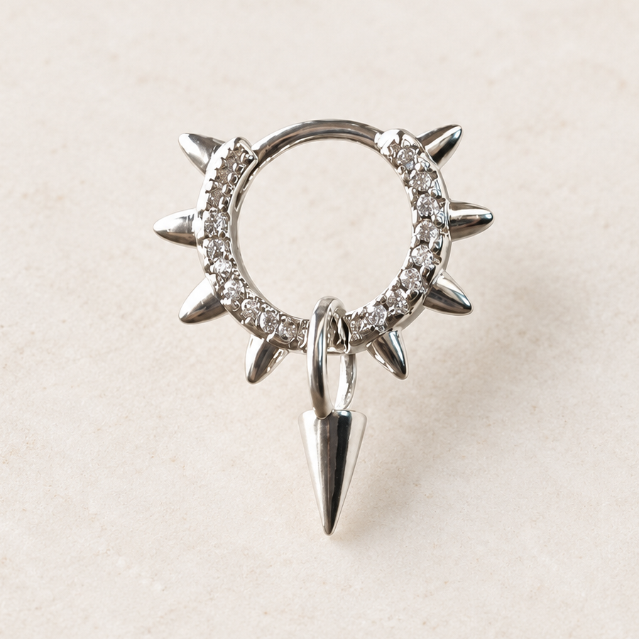 Silver-coloured clear-stone hoop with pointed outer spikes and a hanging spike charm on a pale surface.