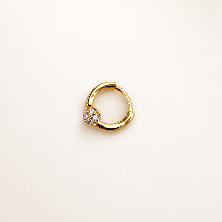 Gold-coloured hinged hoop with a single round clear stone on a pale background.