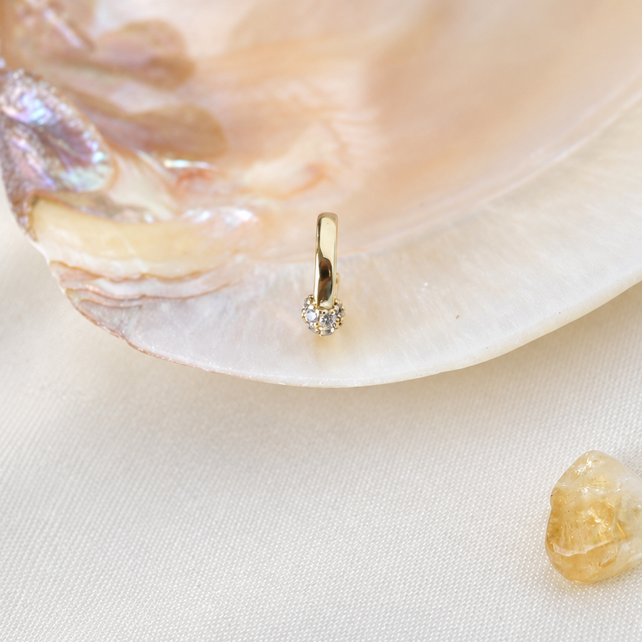 Front-edge view of a gold-coloured clear-stone hoop standing against an iridescent shell.