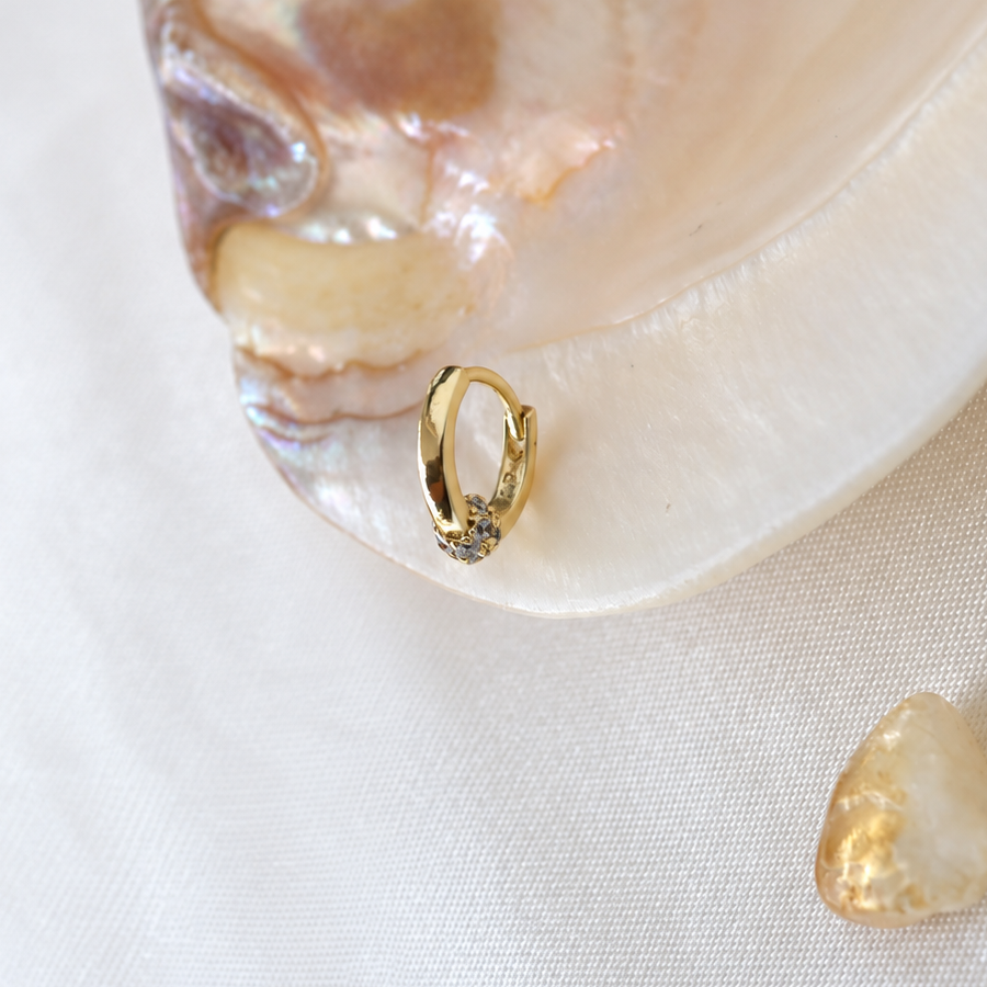 Side view of a gold-coloured clear-stone hoop resting on an iridescent shell.
