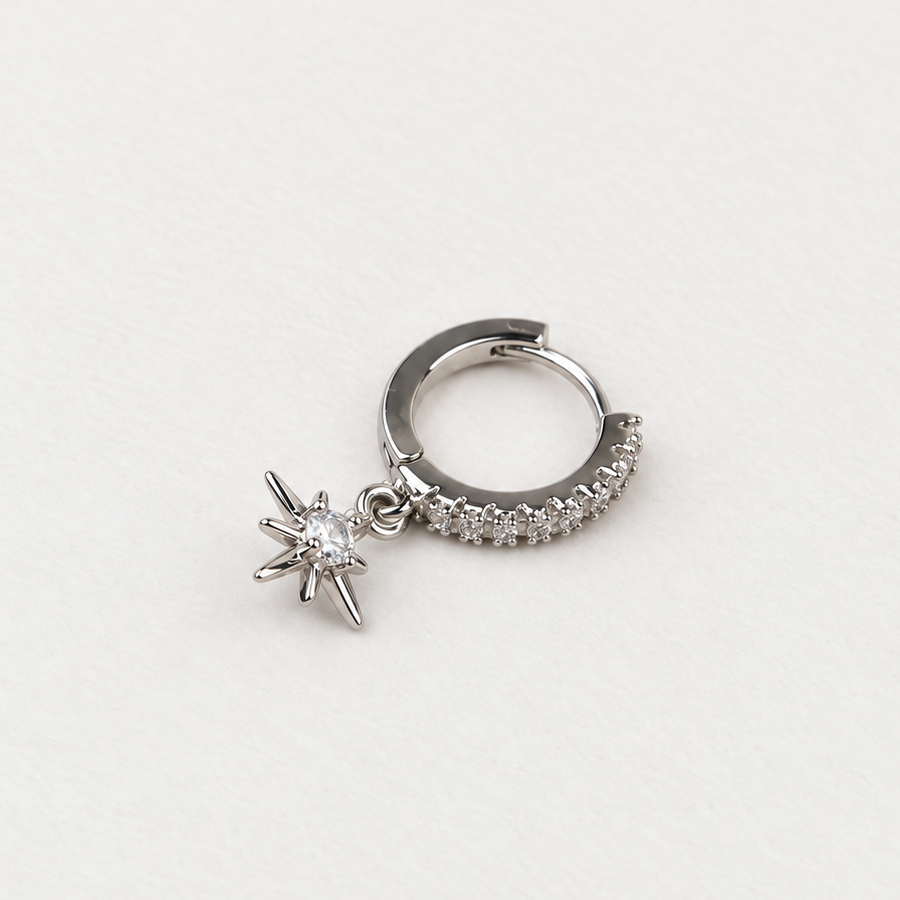 Silver-tone hoop lined with clear stones and a dangling starburst charm on a white surface.