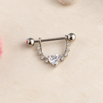 Silver-coloured nipple barbell with a clear heart stone and curved stone-set shield on a pale surface.