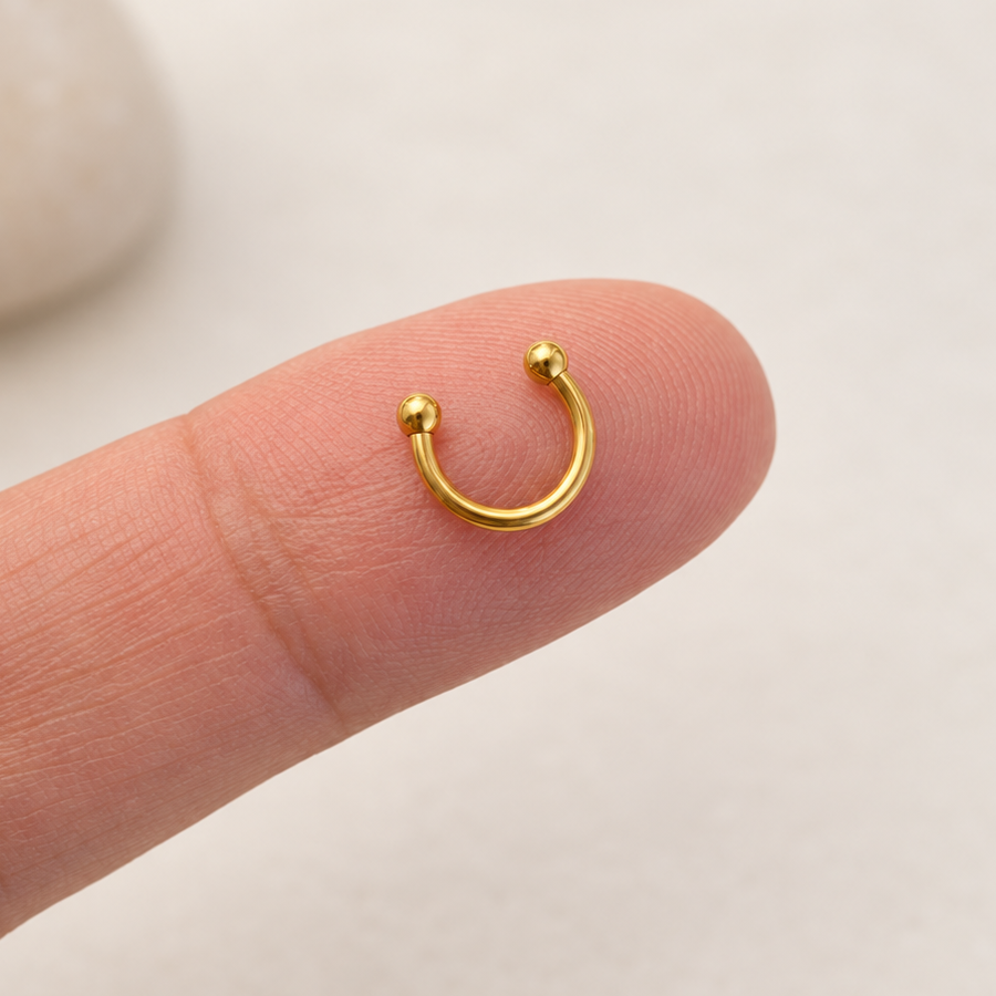 Gold mini horseshoe circular barbell on fingertip