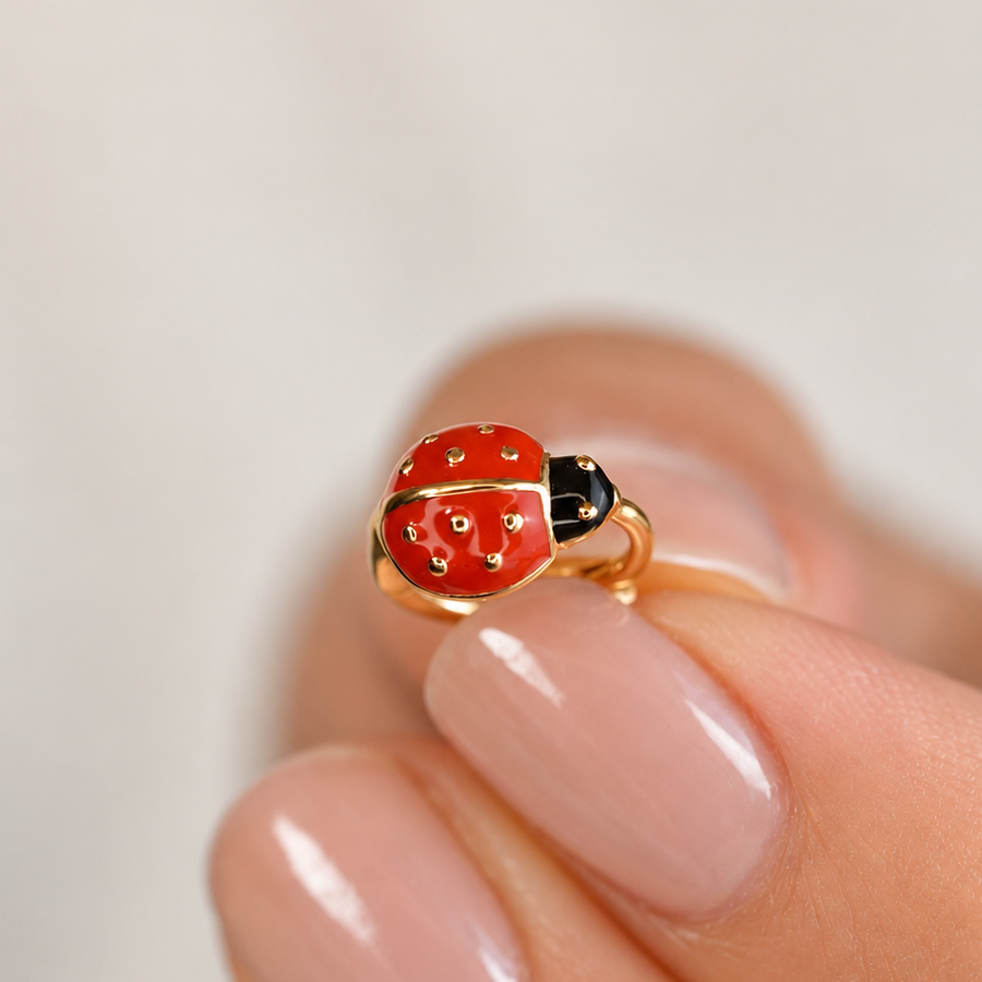 Gold-coloured hoop with a red and black ladybug front held between fingertips.