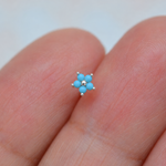 Silver-tone nose stud with five turquoise-blue flower petals and a round centre, displayed on fingers.