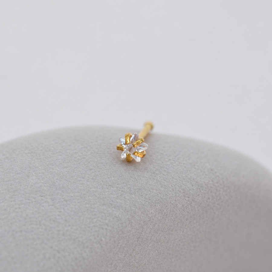 Gold-tone clear-stone nose stud with a straight post resting on a smooth grey pebble.