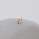 Gold-tone clear-stone nose stud with a straight post resting on a smooth grey pebble.