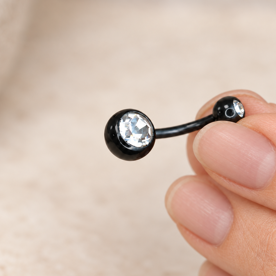 Black curved belly bar held between fingers, with clear stones set in its large and small ball ends.