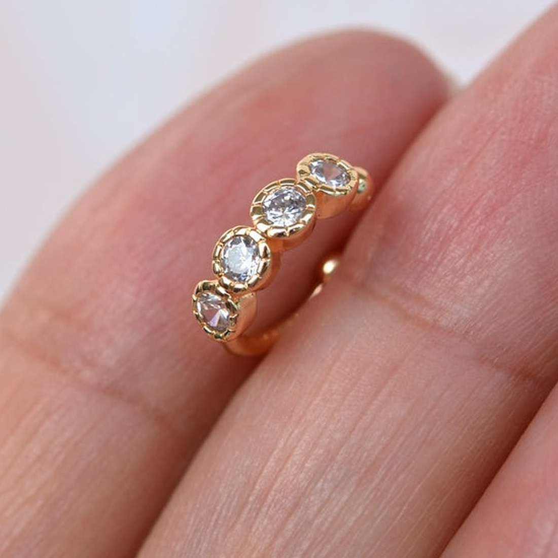 Gold-tone ear cuff with a curved row of four clear round stones resting on fingers.
