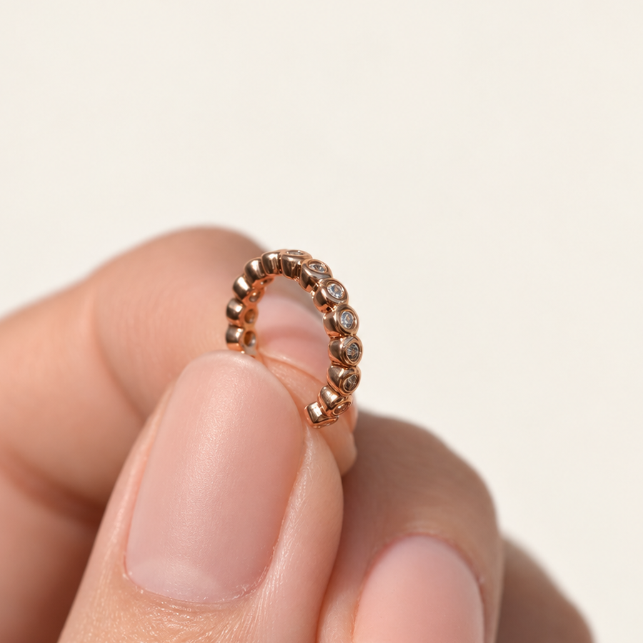 Small warm gold-tone ear cuff held between fingers, with a row of clear round stones and an open gap.