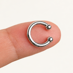 Polished silver-tone ear cuff with two rounded ends and an open gap resting on a fingertip.
