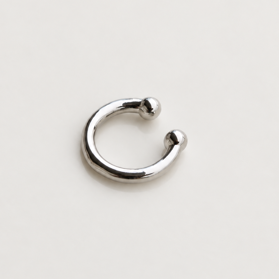 Silver-tone open ear cuff with rounded ends lying on a cream surface.