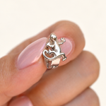 Silver-coloured huggie hoop with a raised lizard design held between fingertips.