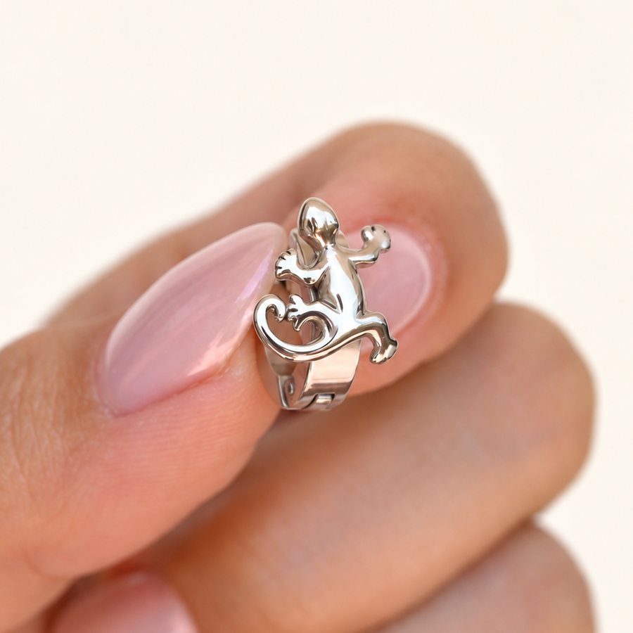 Silver-coloured huggie hoop with a raised lizard design held between fingertips.