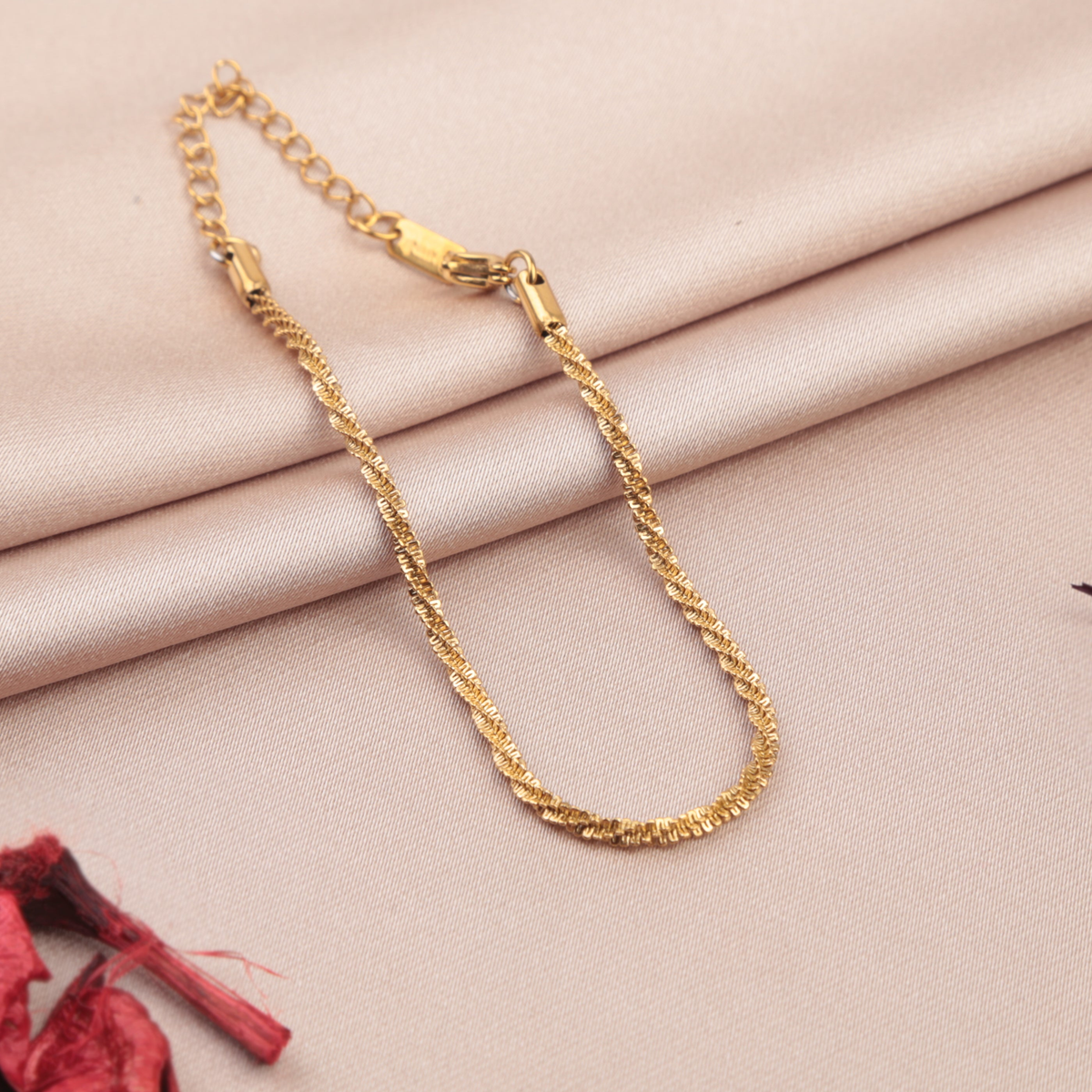 Gold-coloured twisted chain bracelet on folded beige fabric, with its clasp and extension chain visible.