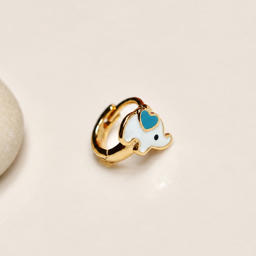 Gold-tone elephant hoop with a white body and turquoise-blue heart detail beside a pale pebble.