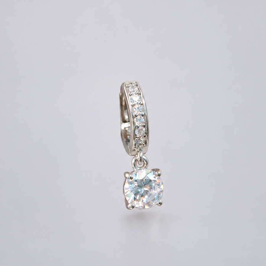 Front view of a silver-tone stone-set hoop earring with a dangling round clear stone on a pale background.