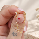 Two gold-tone star studs with clear centres linked by a dangling chain, held between fingertips.