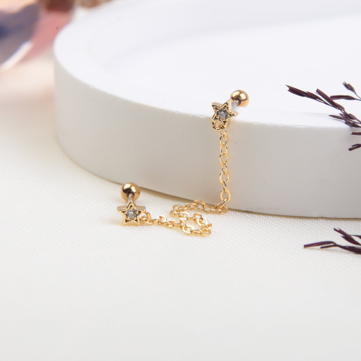 Gold-tone chain-linked star studs with clear centres and ball backs displayed beside a white round tray.