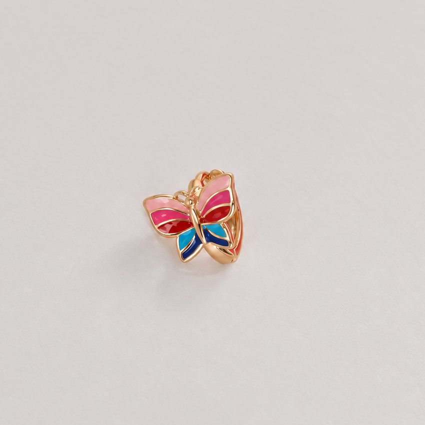Gold-tone butterfly hoop earring with pink, red and blue wings on a pale background.