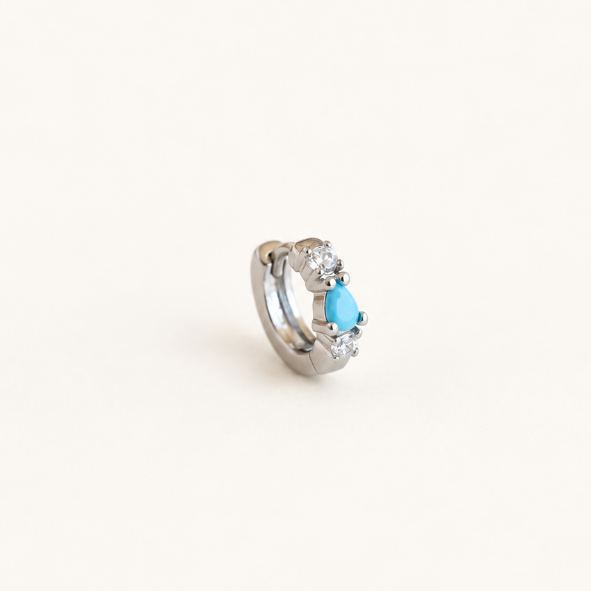Silver-tone hoop earring with a turquoise-blue teardrop centre and clear stones on a pale background.