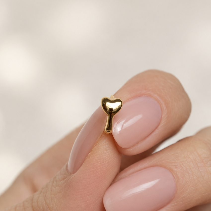 Small gold-tone hoop earring with a polished heart front held between fingertips.